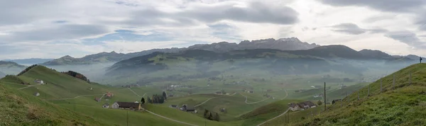 イストのなだらかな丘と農場の背後にある Alpstein 山とスイスの美しいアッペンツェル地域のパノラマ風景を見る — ストック写真