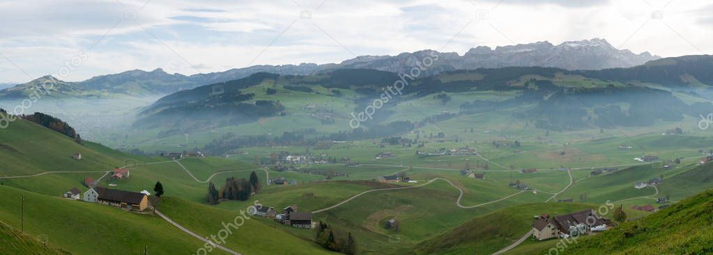 panorama landscape view of the beautiful Appenzell region in Switzerland with ist rolling hills and farms and the Alpstein mountains behind and a lone hiker admiring the view