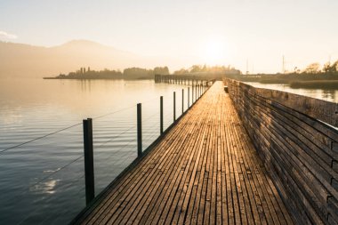Uzun ahşap tahta İskelesi ile bir dağ manzara siluet arka planda altın akşam ışık su üzerinde