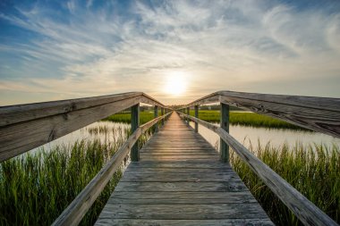 sunset over coastal waters with a very long wooden boardwalk  clipart
