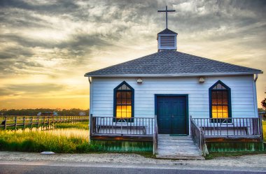 small white wooden chapel on the water on the coast during a colorful summer sunset clipart