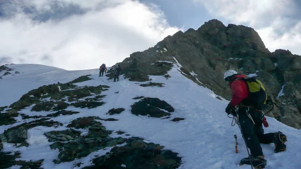 mountain guide leading a climb up a steep rock and snow slope to a high mountain peak