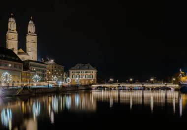 Zürih cityscape Limmat Nehri ile gece ve Grossmuenster Katedrali ve ışıklar ön planda yansımaları ile Köprü