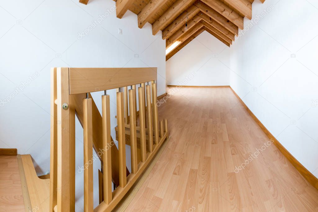 empty spacious and bright attic in a refurbished apartment with wooden parquet floor and white walls and wooden gable roof