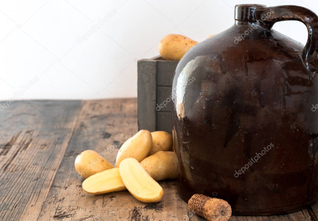 vintage moonshine jug on a rustic wooden table with potatoes and corn cob cork for distilling hard liquor