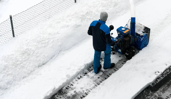 man with a snow blower clears snow from a road after a heavy snowfall in the Swiss Alps in winter