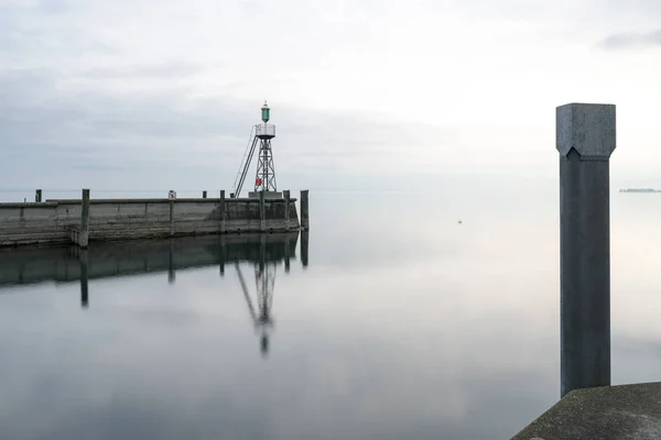 Signal light and harbor wall on calm lake waters under an overca — Stock Photo, Image