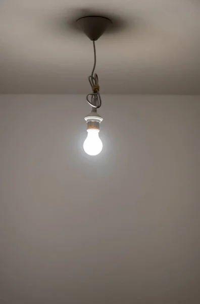 naked lit light bulb hanging from the ceiling of a dimly lit roo
