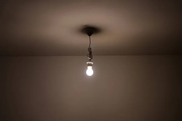 Ampoule allumée nue suspendue au plafond d'une chambre faiblement éclairée — Photo