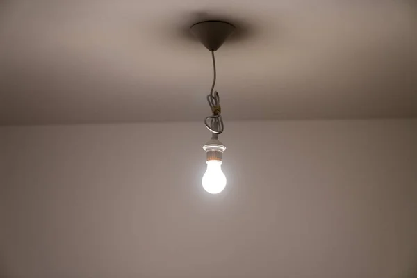 Naked lit light bulb hanging from the ceiling of a dimly lit roo — Stock Photo, Image