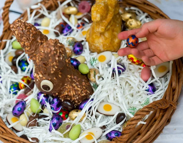 Handen van een kind pak een chocolade snoep ei met een grote Easter Egg basket — Stockfoto