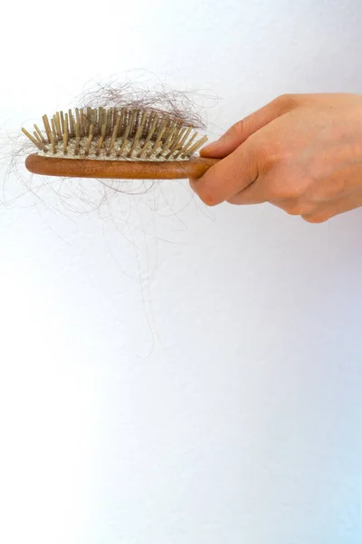 woman holding wooden hair brush full of hair that has fallen out