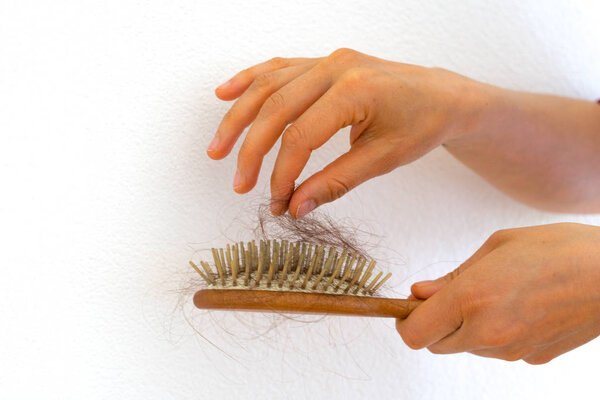 female hands picking hair out of wooden hair brush because of ha