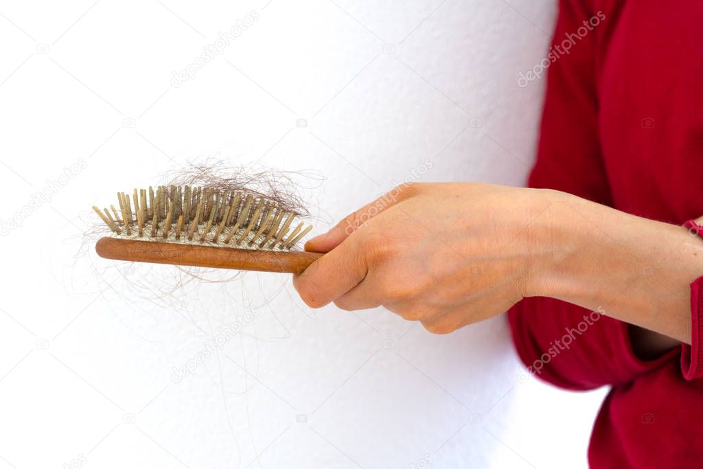 woman holding wooden hair brush full of hair that has fallen out