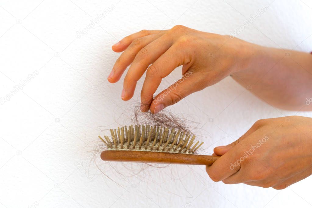 female hands picking hair out of wooden hair brush because of ha