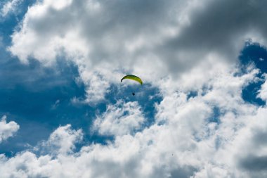 bulutlu ve mavi gökyüzünde sarı bir paraşüt ile yamaç paraşütü