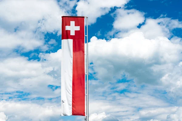 Szwajcarski sztandar flagi pod wyraziste błękitne niebo z białym cumulu — Zdjęcie stockowe