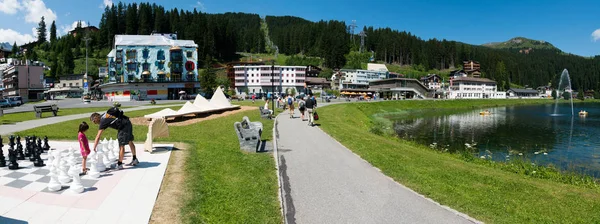 Tourists enjoy summer activities on the lakeshore in Arosa with the train and cable railway station in the background — Stock Photo, Image