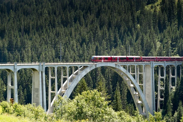 narrow gauge train crosses a long viaduct across a deep ravine in the Swiss Alps