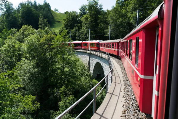 Rojo estrecho ancho tren cruzar sobre un puente de piedra en un st curvilíneo — Foto de Stock