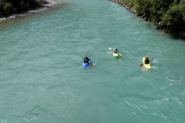 Üç kayakers mavi bir dağ nehirde kürek çekmeye