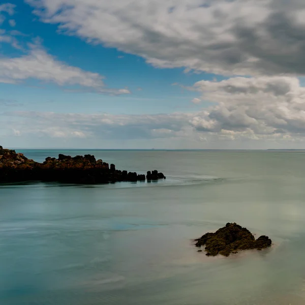 Afloramiento acantilado rocoso en un océano tranquilo bajo un cielo expresivo en t — Foto de Stock