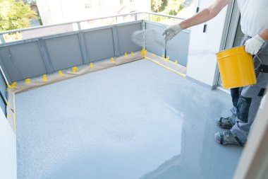 Bir inşaat işçisi balkon zeminini yeniler ve reçineler ve tutkal kaplama üzerine yonga zemin kaplaması yayır
