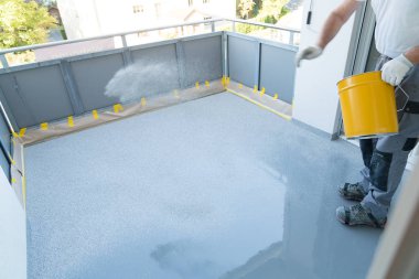 Bir inşaat işçisi balkon zeminini yeniler ve reçineler ve tutkal kaplama üzerine yonga zemin kaplaması yayır