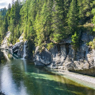 bir dağ gölü ve yeşil çam ormanı ile çevrili küçük şelale ile pastoral manzara