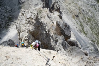 Dağ tırmanışçıları dik ve açıkta bir kaya tepesinde İtalyan Dolomitleri 'nde bir Via Ferrata' ya tırmanıyorlar.
