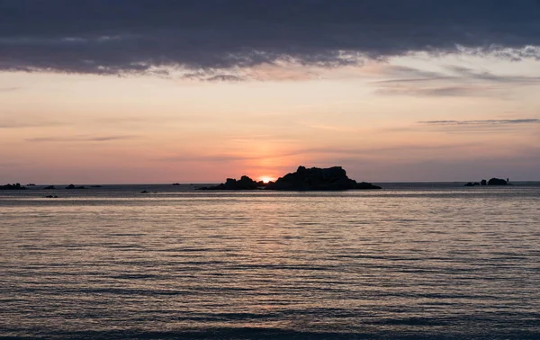 Sonnenuntergang am Strand mit einem ruhigen Meer und Felsen und Riffen unter einem orange-blauen Himmel — Stockfoto