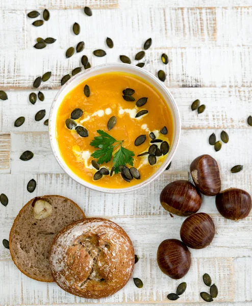Kestane ve kestane ağacının çerçevelediği beyaz bir kasede organik kabak çorbası.
