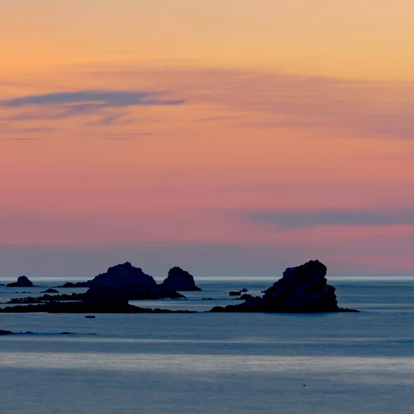 Por do sol na praia com um oceano calmo e rochas e recifes sob — Fotografia de Stock