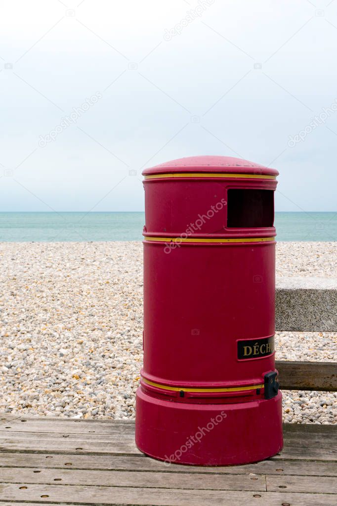 large vintage red trash can on a wooden boardwalk at a rocky beach