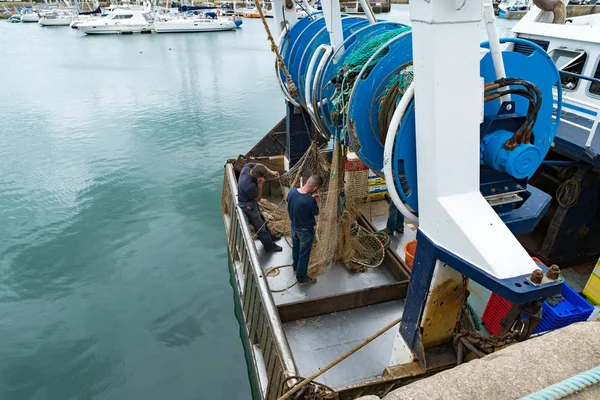 Fishermen repair fishing nets on their fishing boat in the harbor — Stock Photo, Image