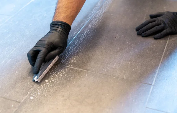 Profesyonel temizlik malzemesi, fırça bıçağı ve köpüklü sabunla gri fayanslı bir banyonun zemininde.