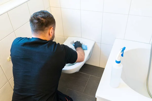 A professional cleaner cleans a ceramic toilet very thoroughly in a modern bathroom