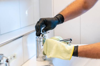 Profesyonel bir temizlikçi banyo lavabosunu ve musluğu sarı bir mikro fiber bezle parlatır.