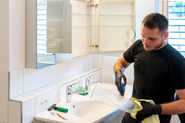 Banyoyu temizleyen profesyonel bir temizlikçi ve banyo dolabındaki cam raflar.