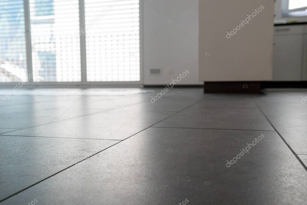 A low angle horizontal view of a new black ceramic tile floor in a bright white light apartment