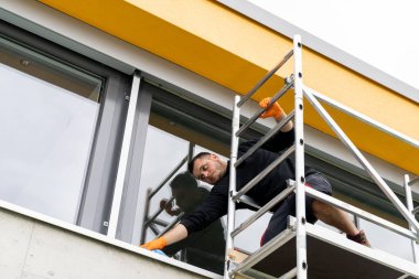 Taşınabilir bir iskele üzerindeki pencere temizleyicisi bir evin pencerelerini temizliyor.