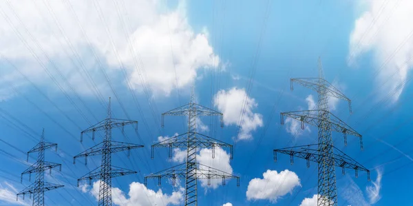 白い雲と光霧を持つ青い空の下で電気を輸送するいくつかの大きな金属高電圧格子交差 — ストック写真