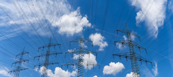 白い雲と青い空の下で電気を輸送するいくつかの大きな金属高電圧格子交差 — ストック写真