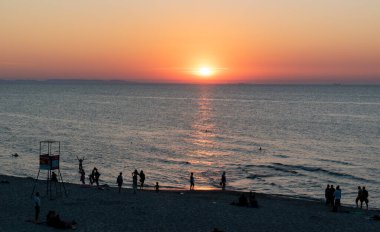 Polonya 'da Baltık Denizi' nde gün batımının keyfini çıkaran birçok insanın silueti.