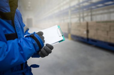 Closeup shooting hand of worker with clipboard checking goods in freezing room or warehouse clipart