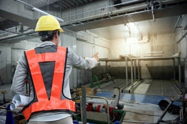 Sabit şapkaile çalışan ve elinde plan tutan mühendislere danışmanlık yapan mühendisler.,Otopark binasında inşaat denetçisi işleri.