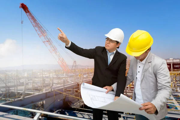 Management consulting with engineers working with hard hat and holding blueprint in his hand for management business plan.