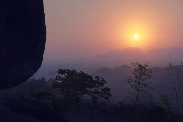 Sunrise in the mountains with silhouette a stone is foreground.