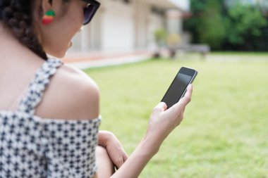 Asyalı kız oturuyor ve bahçede cep telefonu kullanıyor. Sosyal ağ hizmeti kavramı.