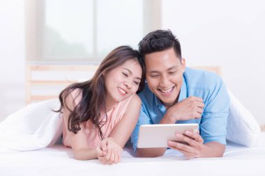 Yatak odasında yatakta yatarken tablet kullanan genç bir çift..